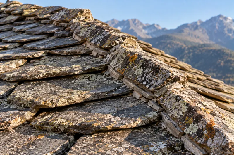 Toiture en lauzes de pierre couvertes de lichen, montagnes à l’arrière-plan